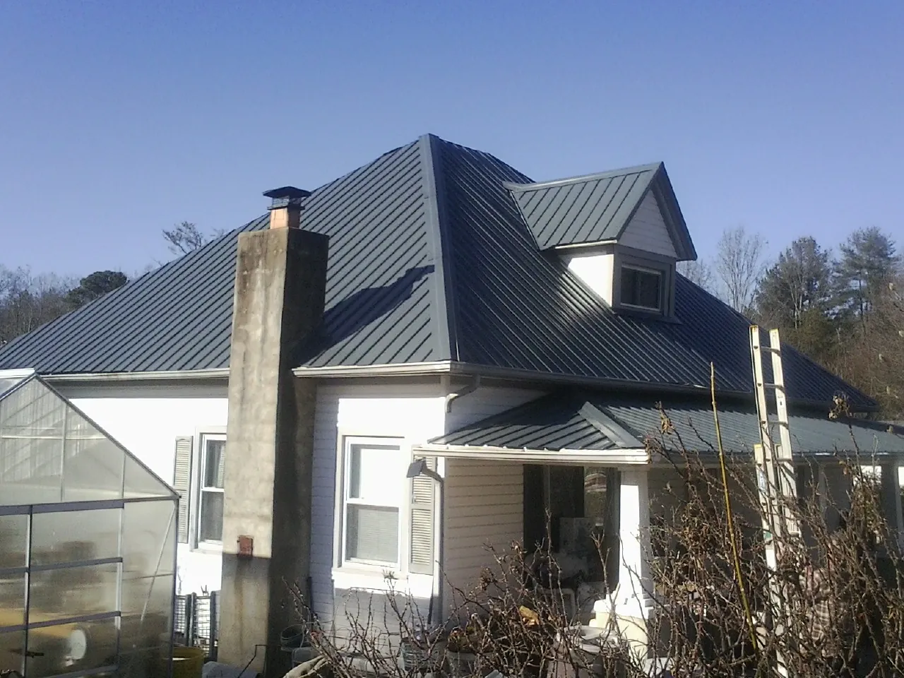 Dark blue standing seam metal roof on a white farmhouse with dormer — Slate & Tile Roof Repair by Roofing Brothers in Summerfield